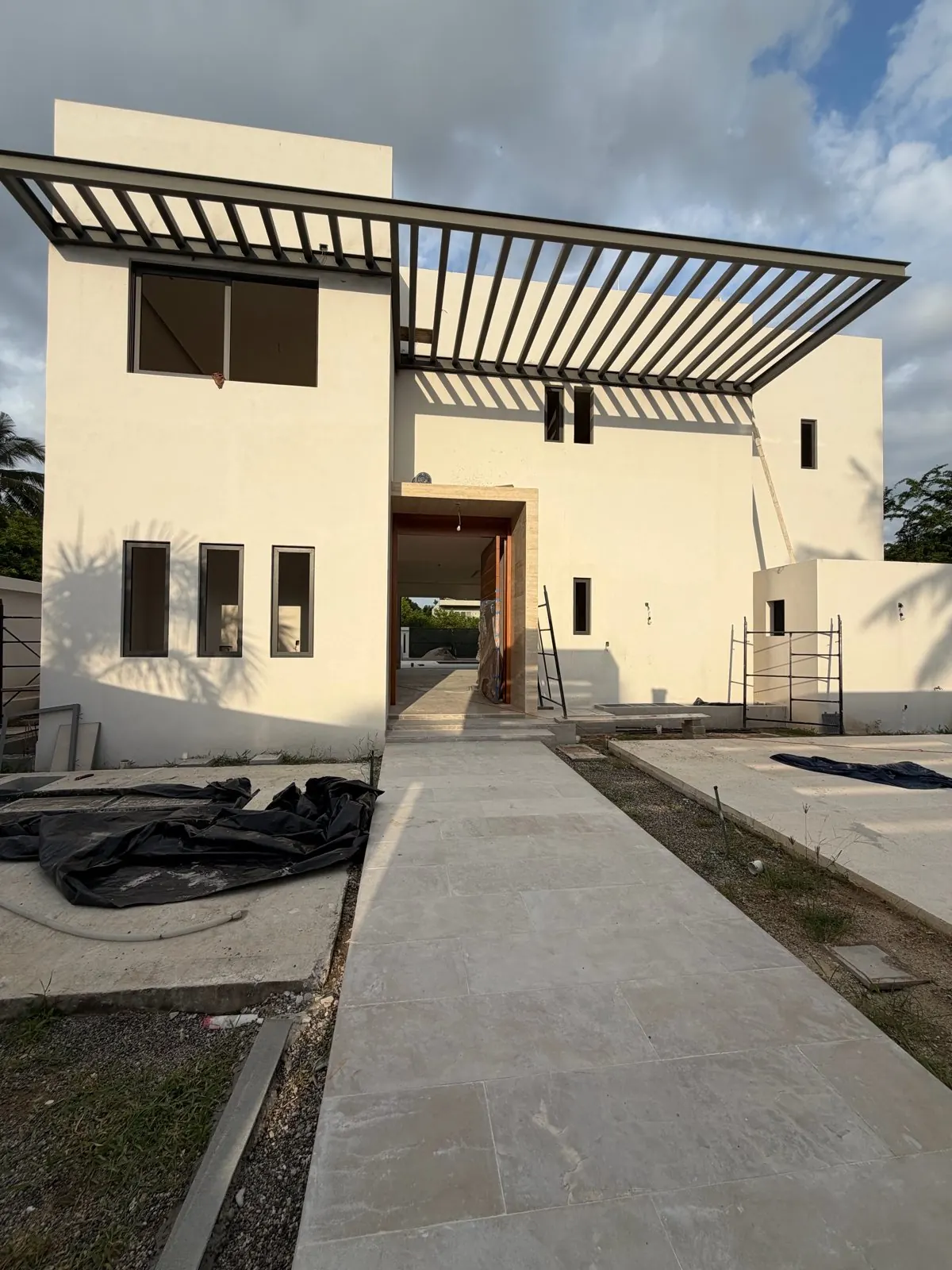 Real photo, Oct 2026. Facade of the house under construction at dusk, with floor-to-ceiling windows and a set-back upper floor.