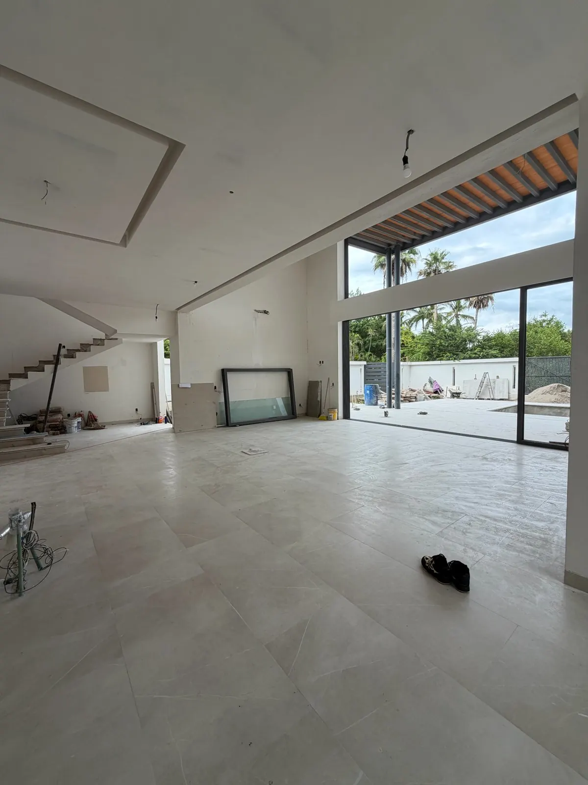 Real photo, Oct 2026. Double-height living room with the stair, large-format tile and glass doors toward the terrace.