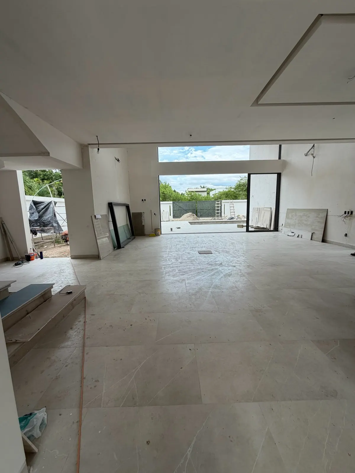 Real photo, Oct 2026. Interior toward the terrace: large-format tile, sliding doors and the pool under construction.